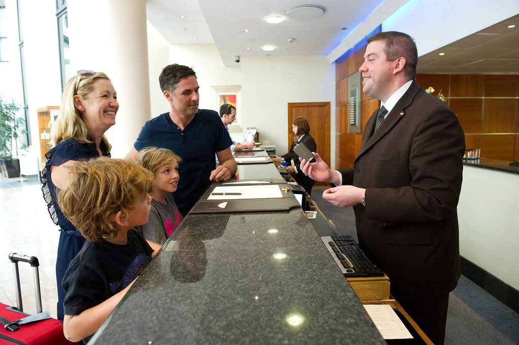 A family at a hotel reception desk; the receptionist smiles and gives them a room key card
