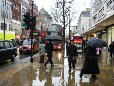 A rainy street in London with red buses, a black taxi and people with umbrellas