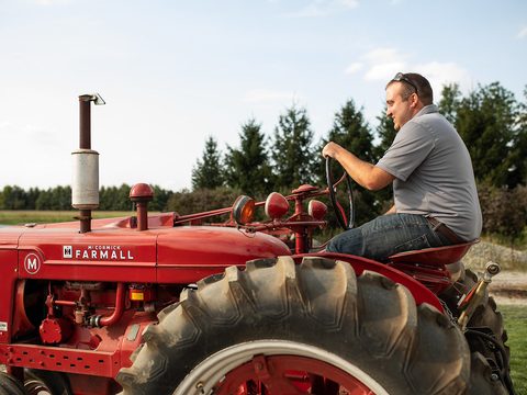 A man driving an old red tractor on a farm