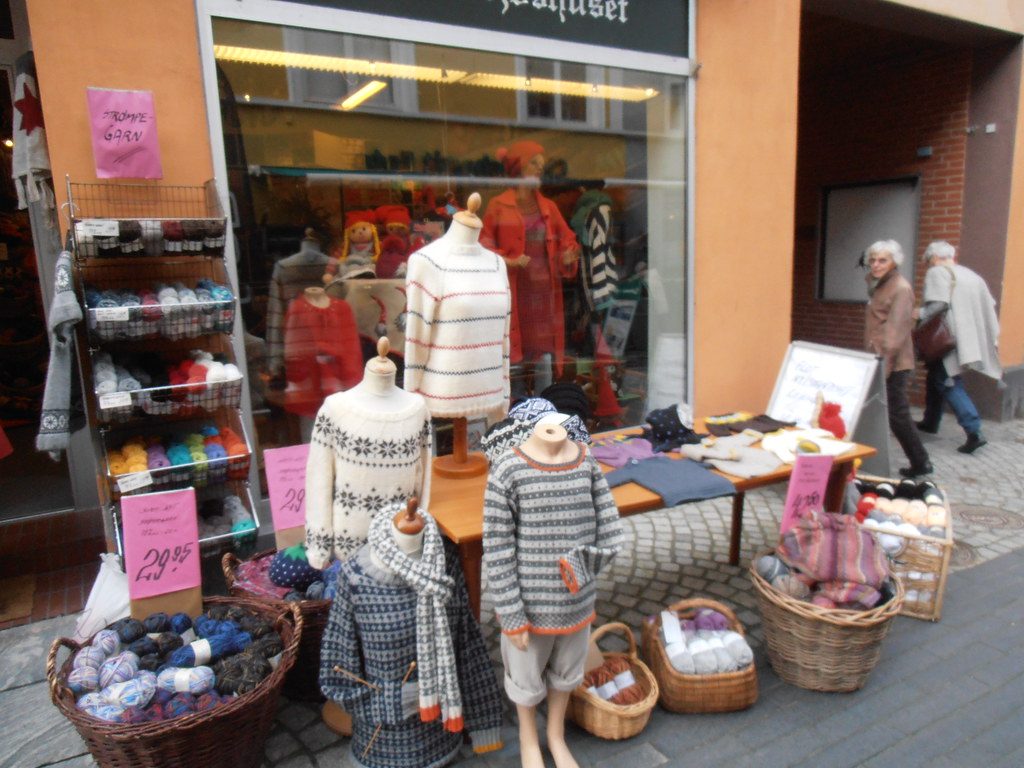 A yarn store with baskets and racks of yarn on the sidewalk and knitted sweaters on mannequins