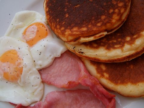 Pancakes, two fried eggs and slices of bacon on a plate