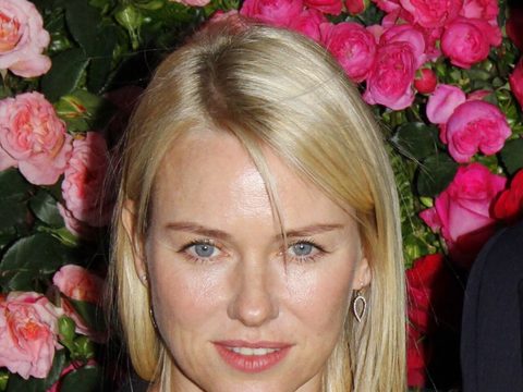 Naomi Watts, smiling, in front of pink roses