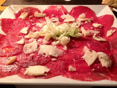 Thin slices of raw red beef with white cheese and green salad on a white plate