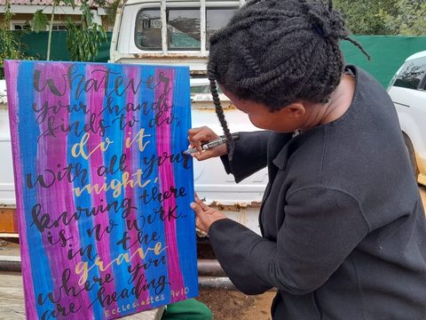 A woman writes big colorful letters on a canvas with a pen