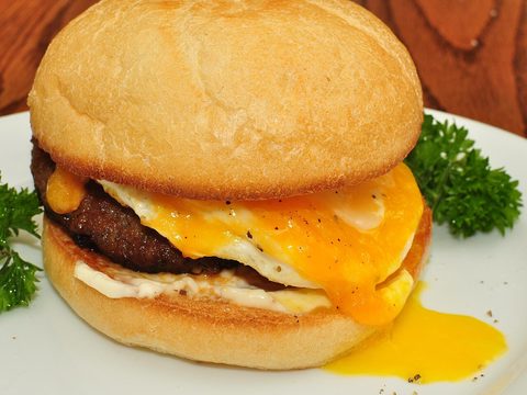 A sandwich with sausage, a fried egg and cheese on a white plate
