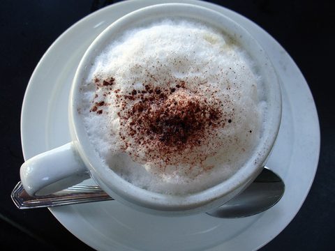A cappuccino in a white cup with thick milk foam and cocoa powder on top