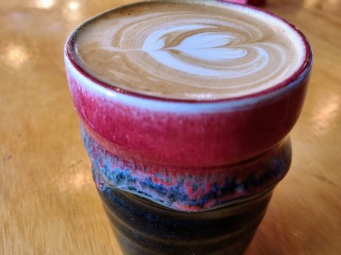 A hot latte with a heart on top, in a red and blue cup
