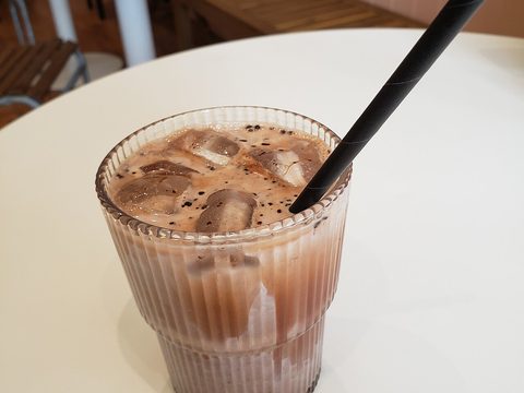 An iced mocha in a tall glass with ice and a black straw