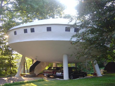 The Spaceship House, a round white house on tall pillars, with two cars parked underneath