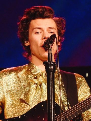 Harry Styles singing and playing the guitar in a gold jacket