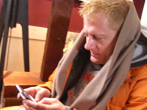 A man in a scarf typing a message on his cell phone