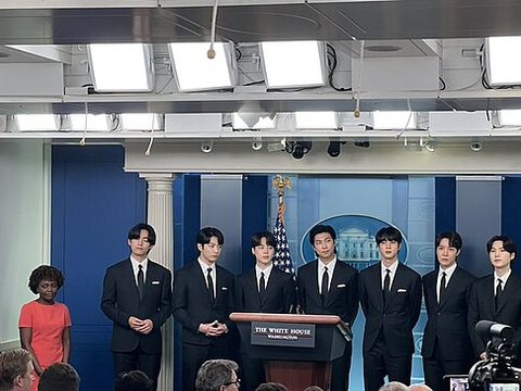 The seven members of BTS in black suits, standing in a line at the White House