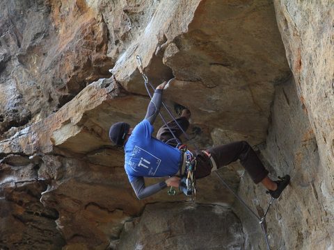 A man in a blue T-shirt climbing a big rock