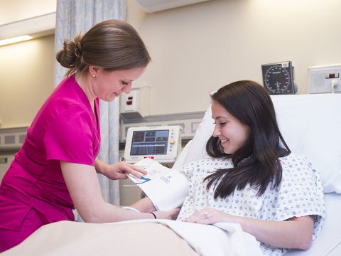 A nurse in pink scrubs talking to a smiling patient in a hospital bed